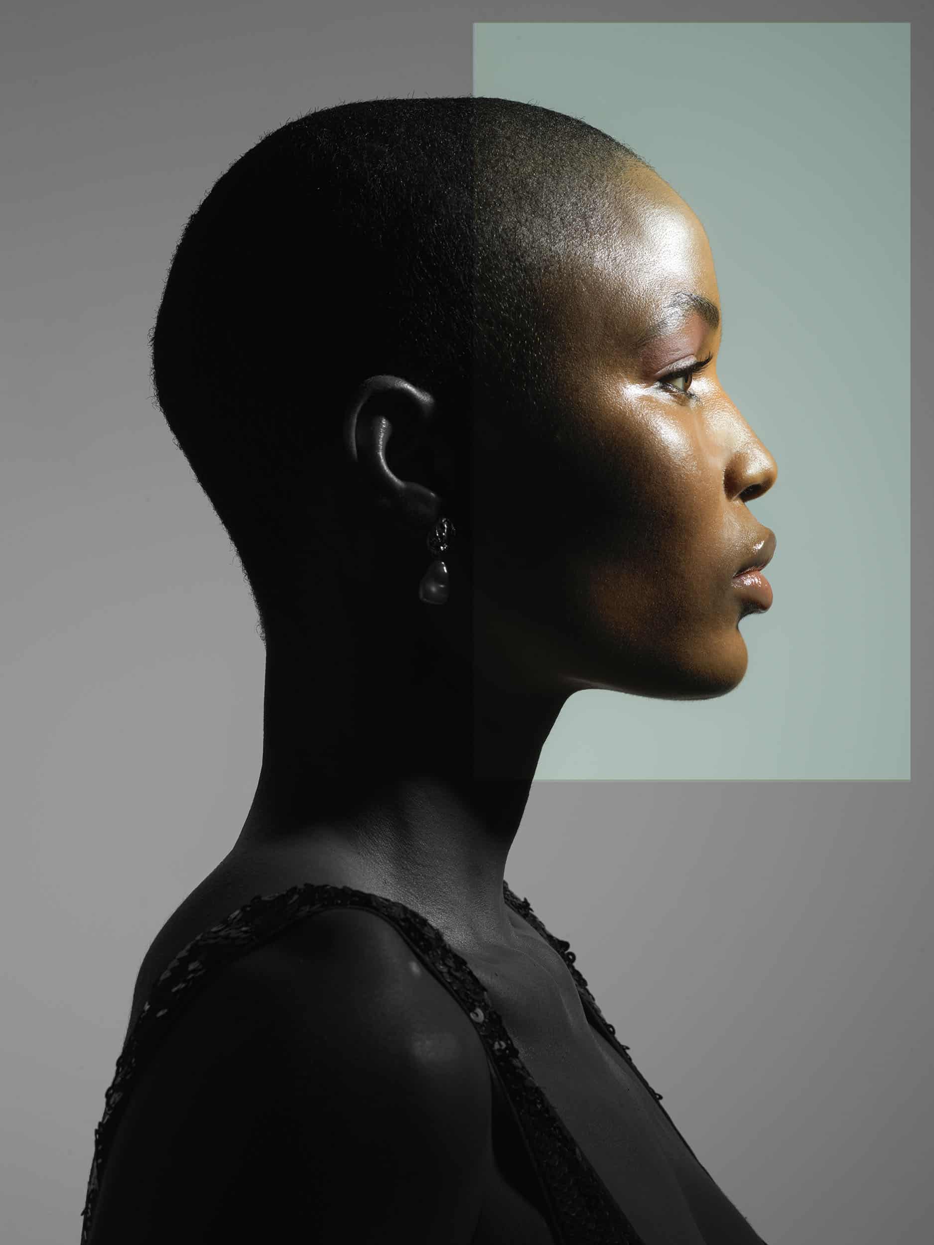 Side profile of a black women with a shaved head, with one half of her face in colour and the other half in black and white