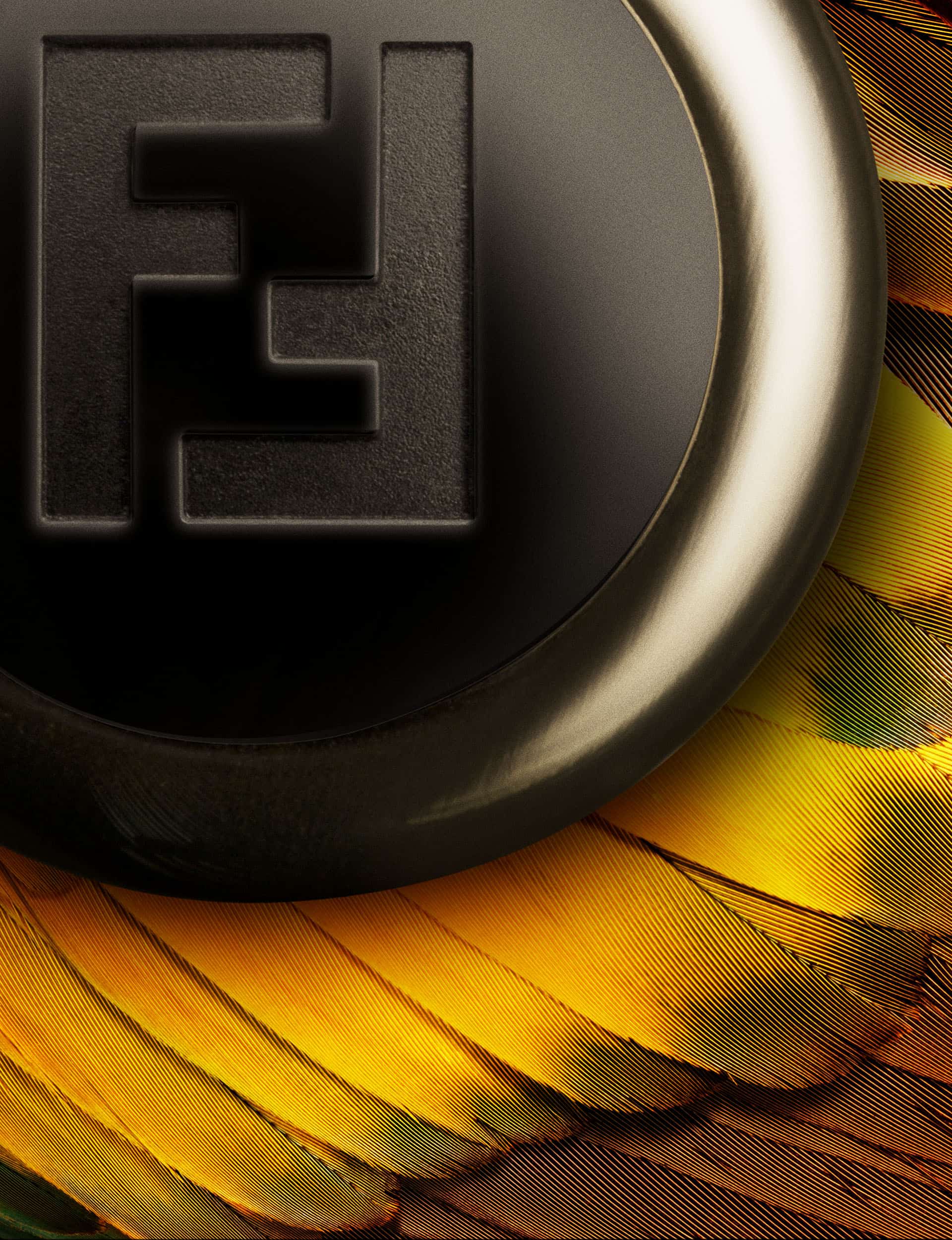 Close up macro shot of the Fendi perfume bottle with the logo embossed on it. This sits on a bed of yellow and orange parrot feathers.