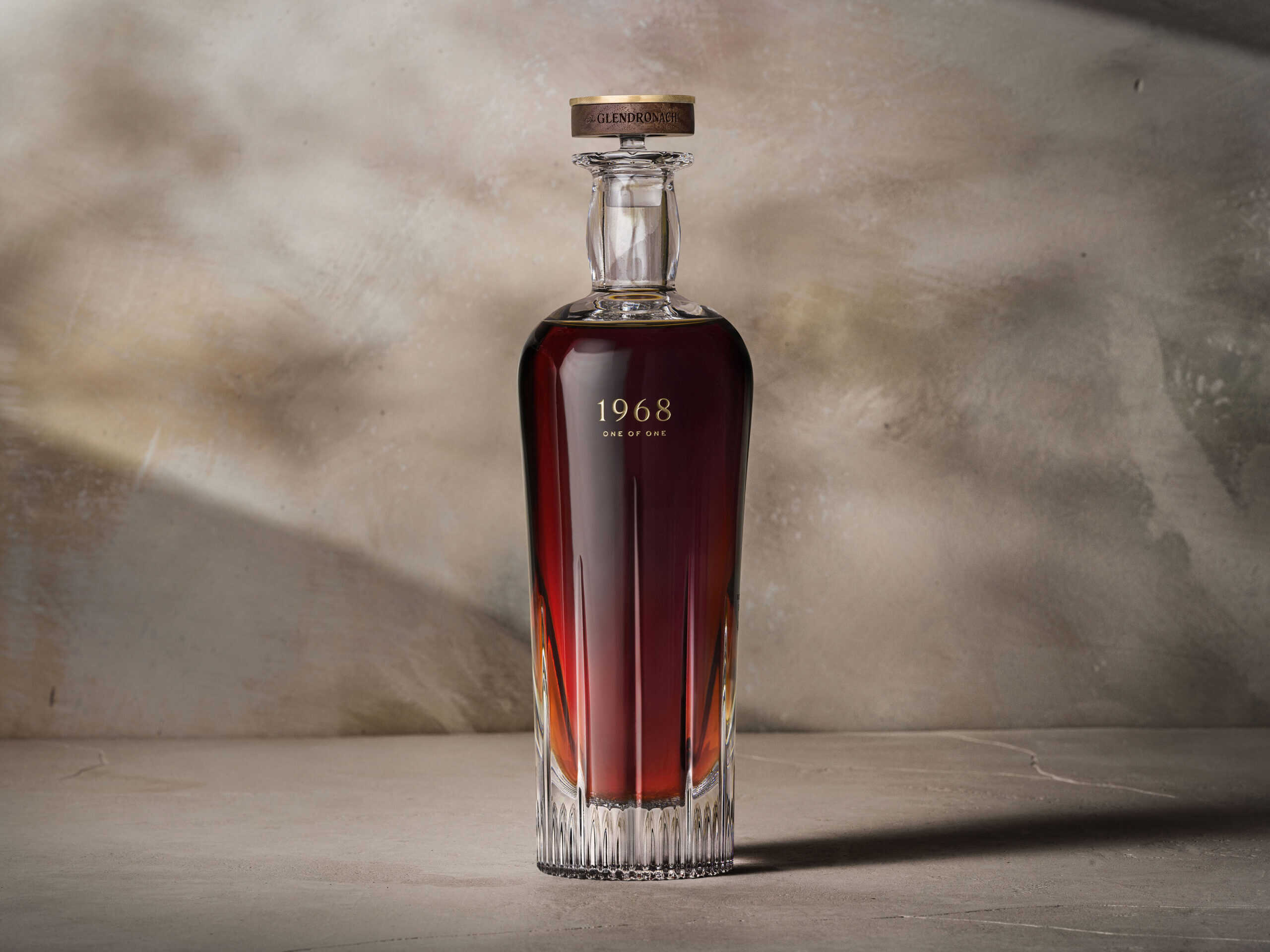 One bottle of Glendronach whisky sitting on a neutral stone background and surface. A single shaft of light highlights the bottle.