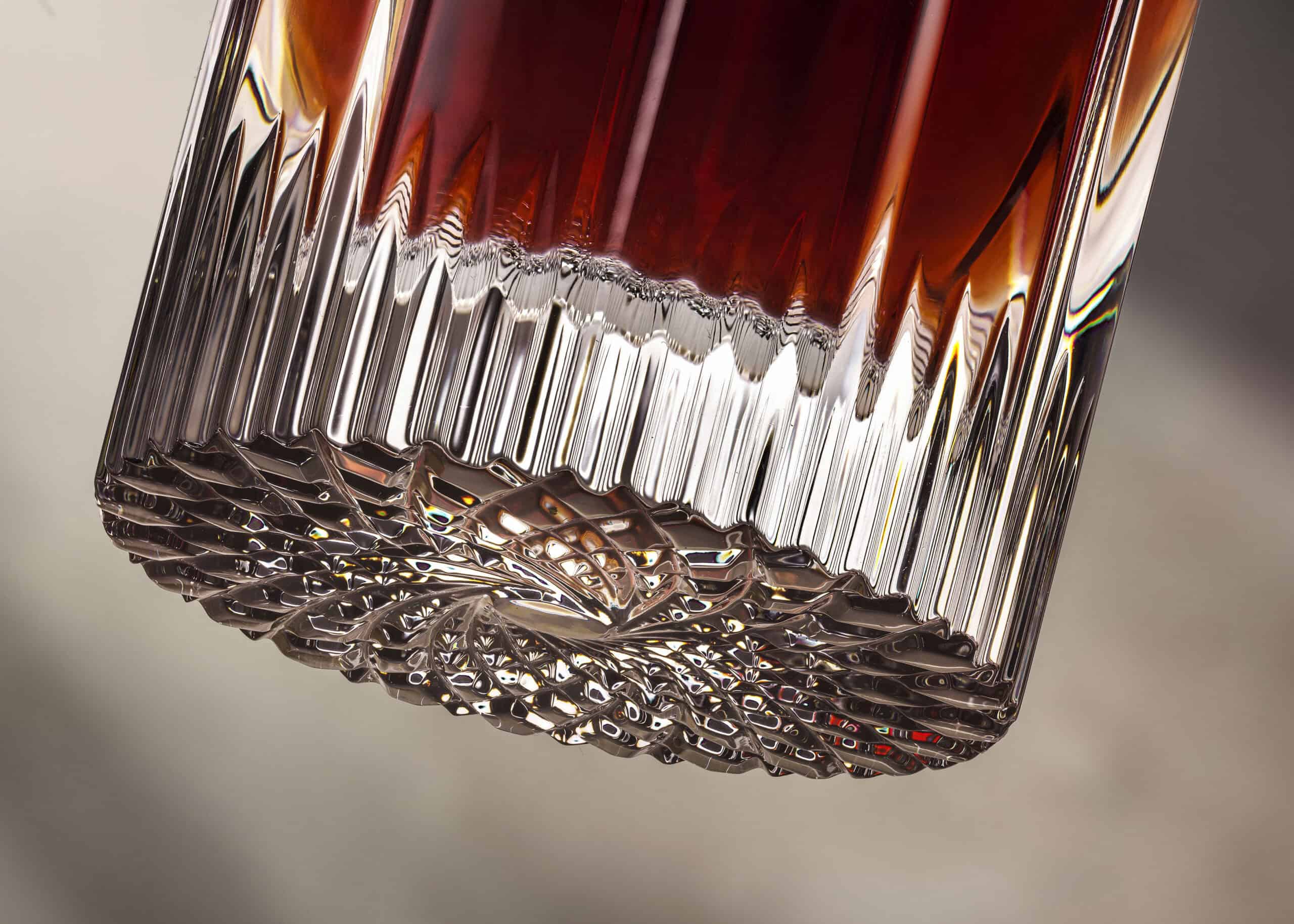 Close-up of a glass base of a bottle of Glendronach whisky as though suspended in the air with a neutral stone background behind the bottle.