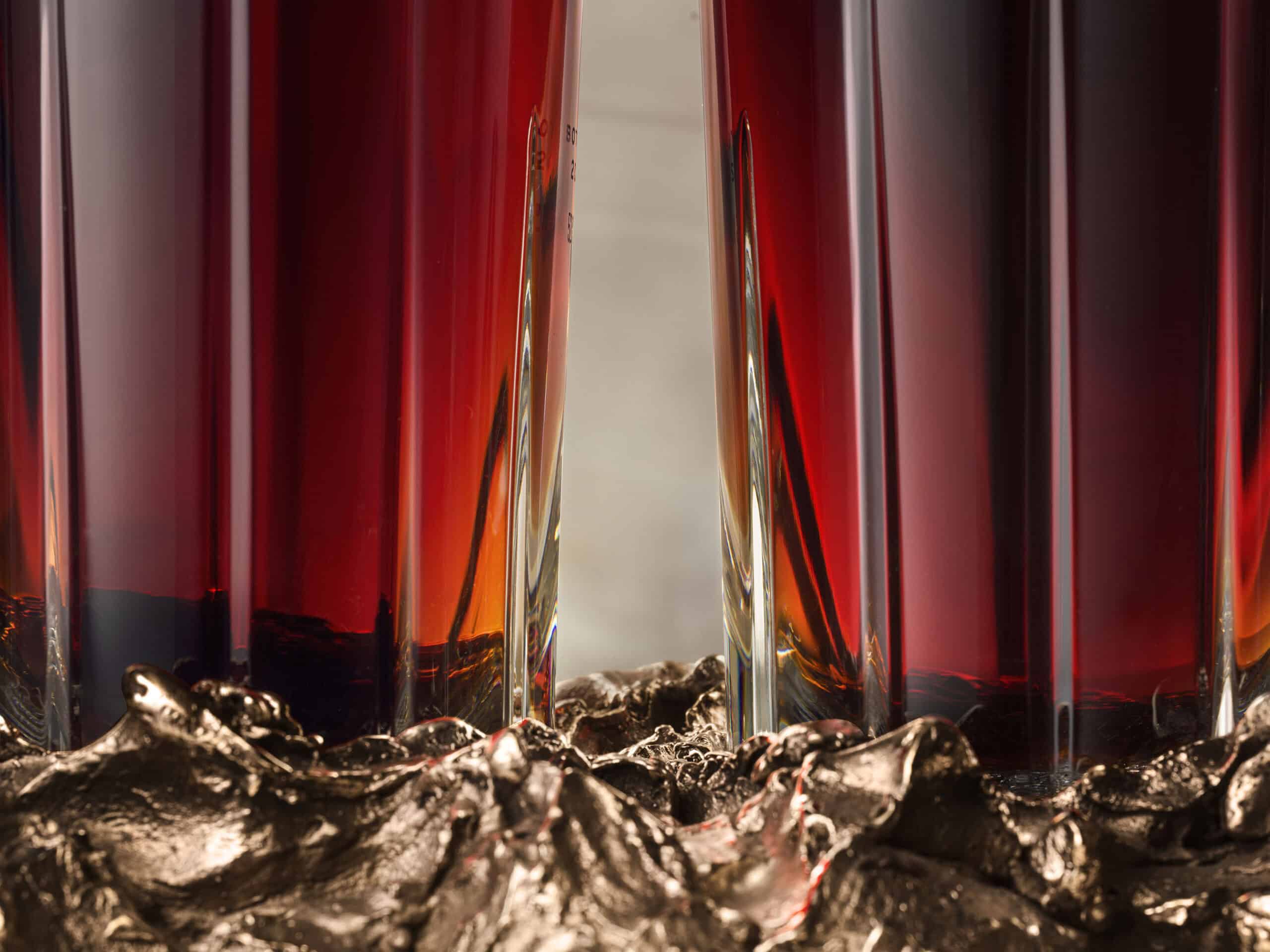 Close-up of the base of two bottles of Glendronach whisky sitting in a bronze sculpture on a neutral background.