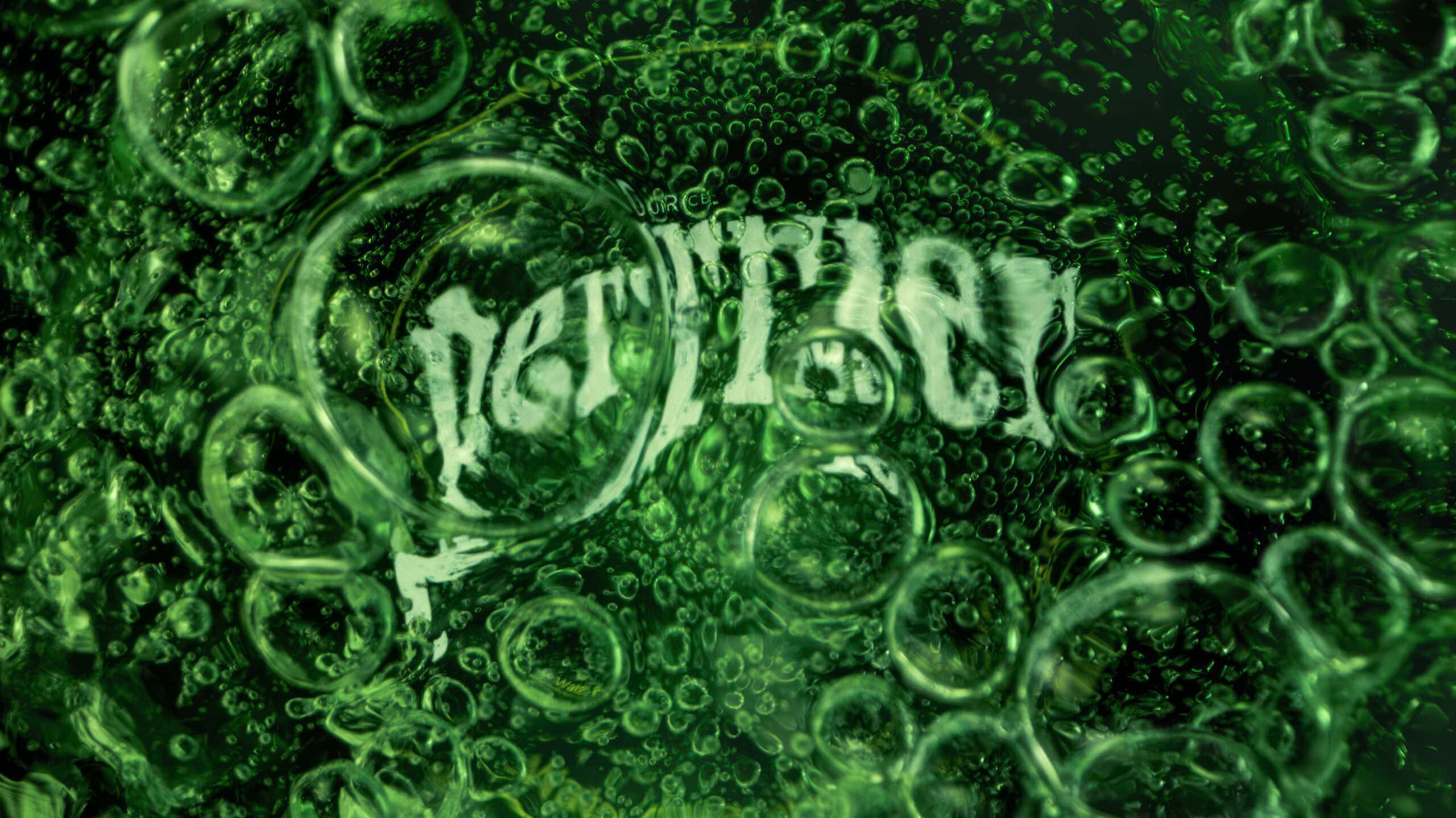Macro image inside a green glass bottle of Perrier sparkling water. In the centre of the image you see the bottom of the glass with the word 'Perrier' written which has bubbles covering the logo.