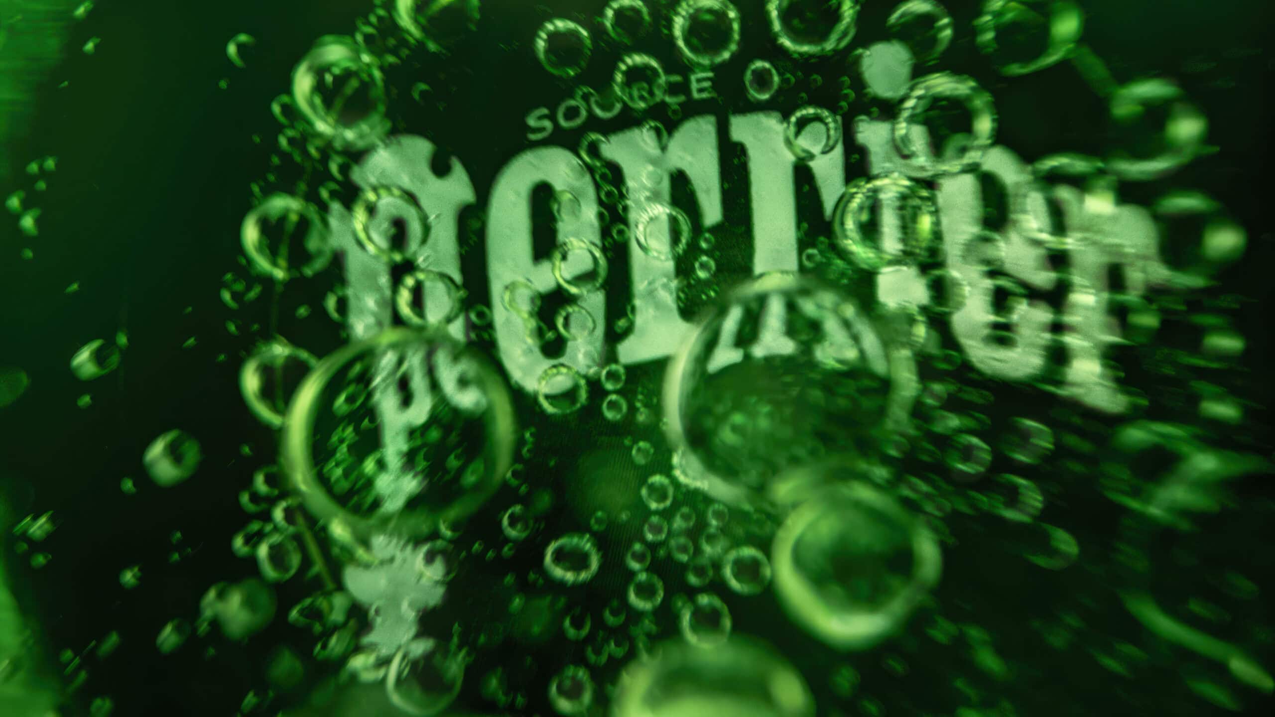 Macro image inside a green glass bottle of Perrier sparkling water. In the centre of the image you see the bottom of the glass with the word 'Perrier' written which has bubbles covering the logo.
