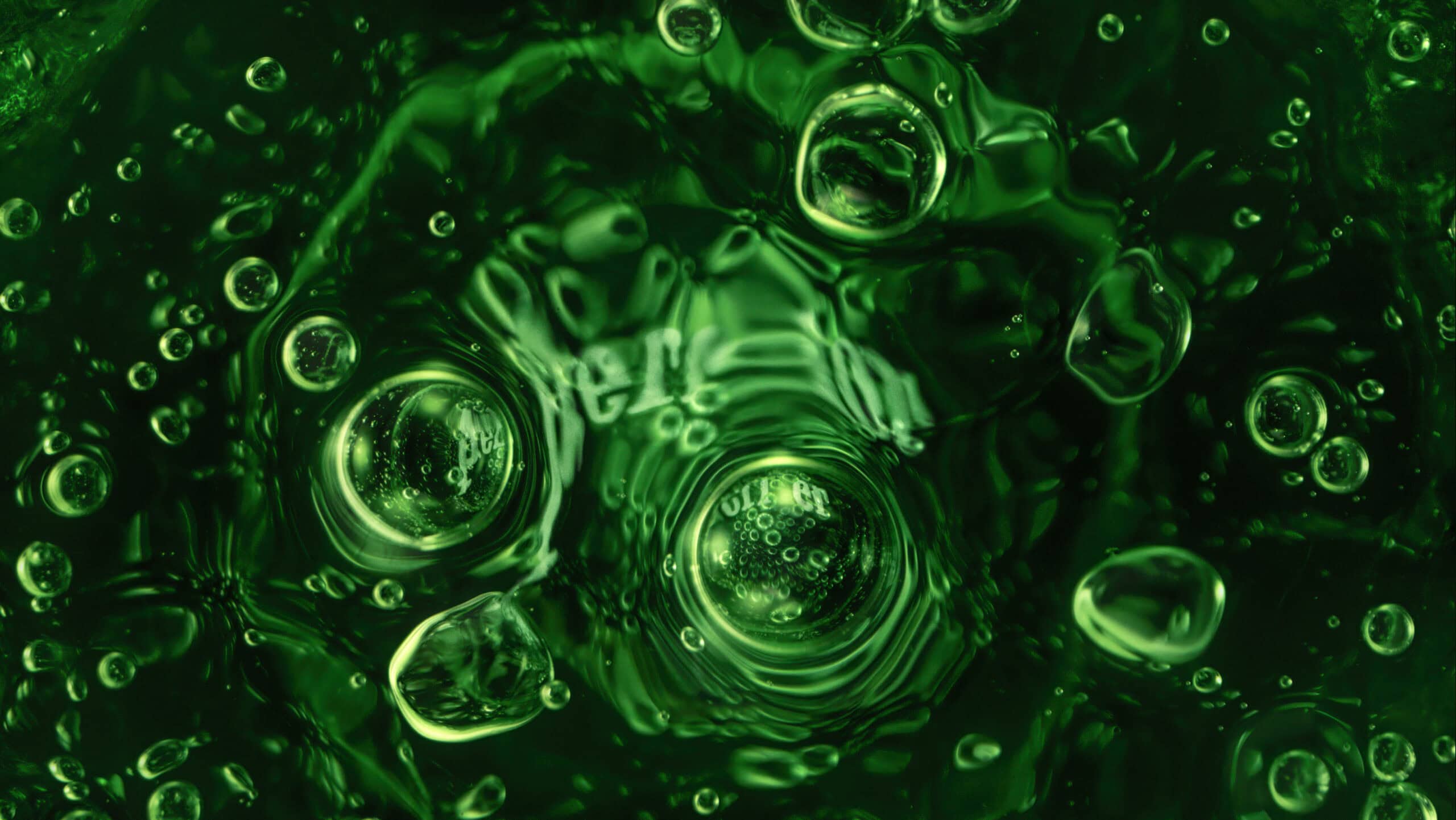 Macro image inside a green glass bottle of Perrier sparkling water. In the centre of the image you see the bottom of the glass with the word 'Perrier' written which has bubbles covering the logo.
