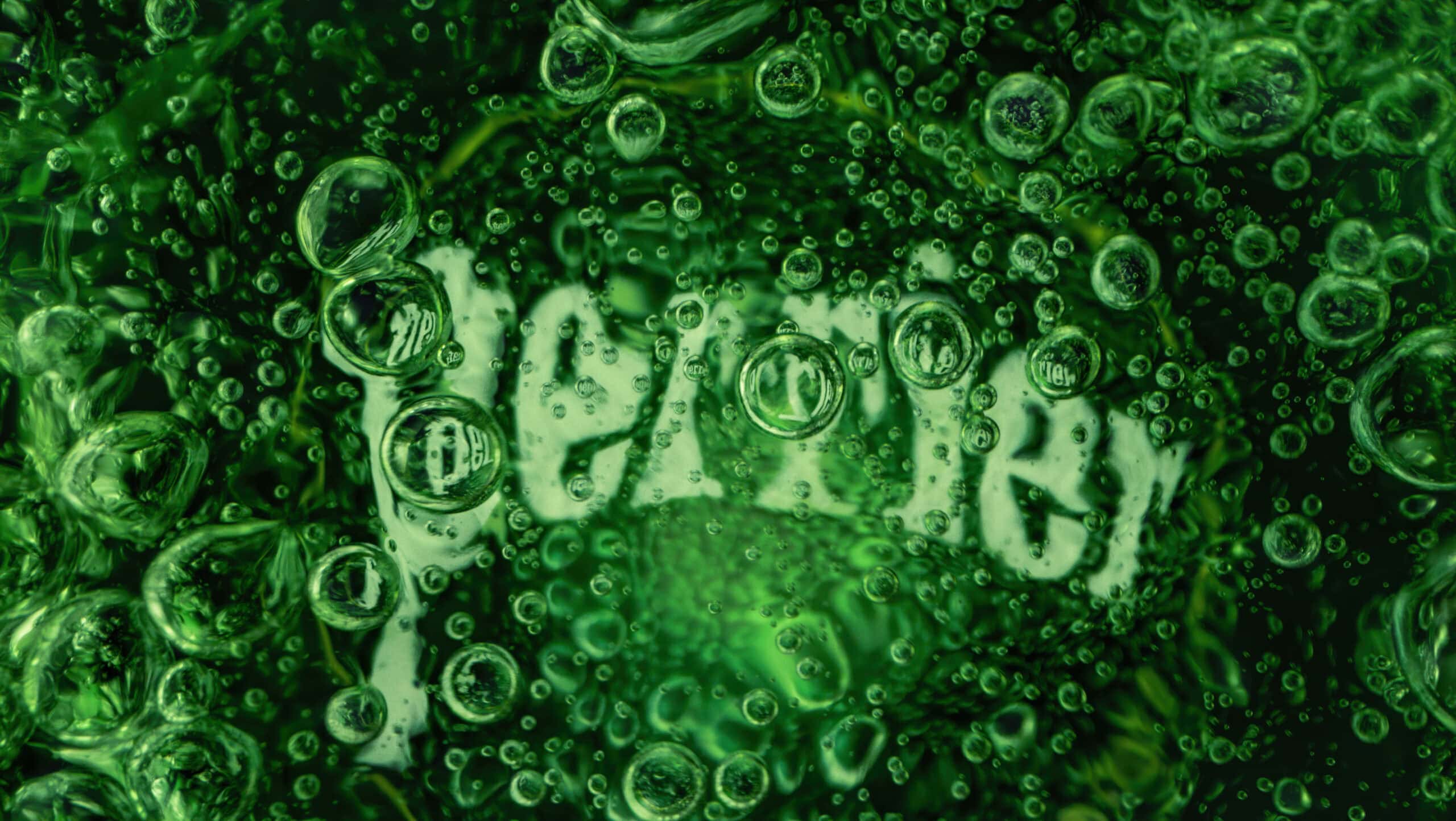 Macro image inside a green glass bottle of Perrier sparkling water. In the centre of the image you see the bottom of the glass with the word 'Perrier' written which has bubbles covering the logo.