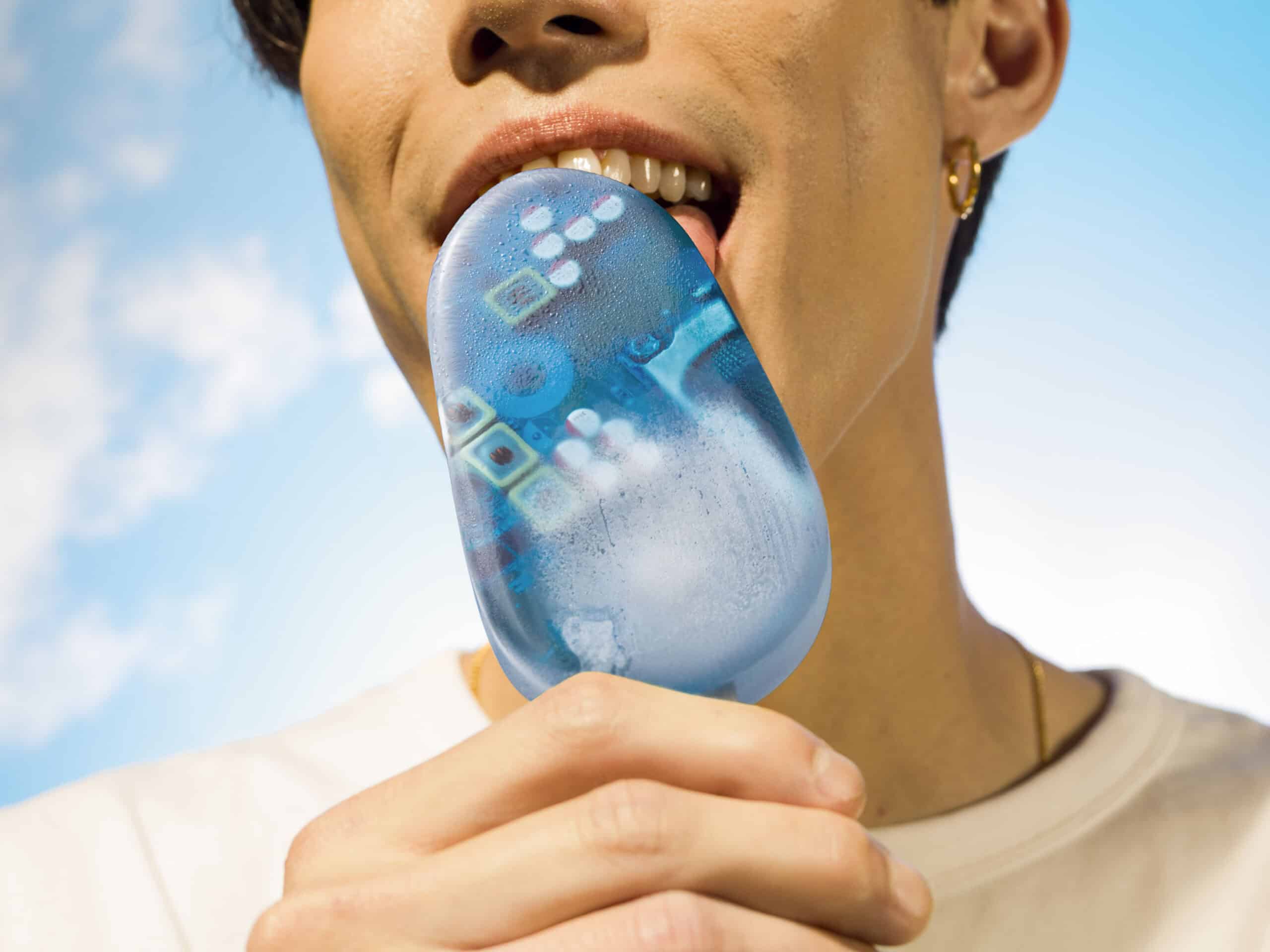Close up of an Asian male in mid-20's licking a blue ice lolly that has tech chips placed inside. The background is a sunny blue sky
